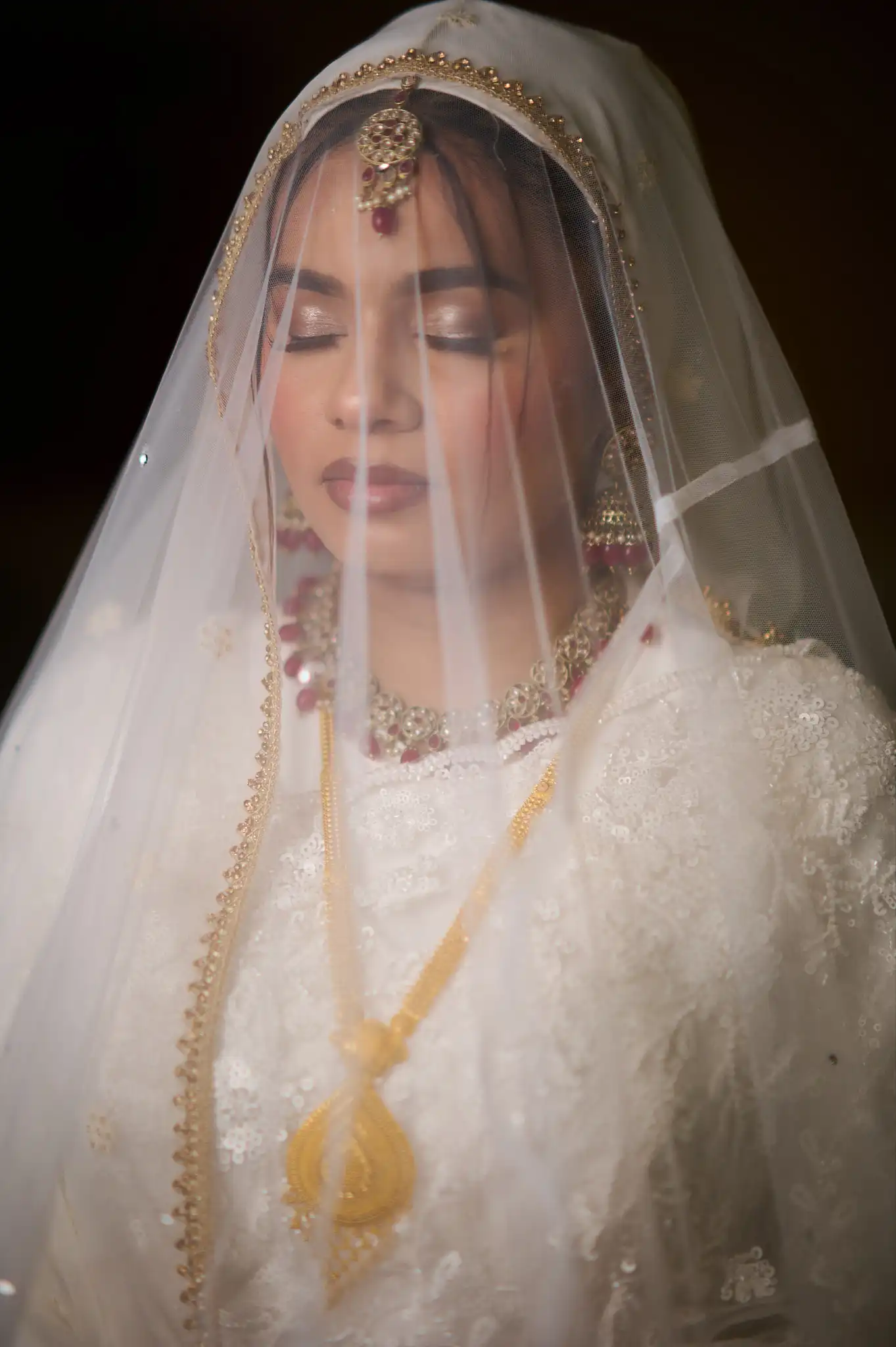 Bride in mint green and gold outfit framed by white roses in soft foreground focus